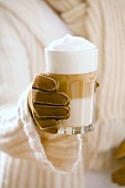 Frau mit Handschuh hält ein Glas Latte Macchiato