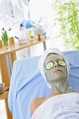 Woman with clay face mask and cucumber slices on her eyes