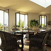 Esstisch mit Rattansesseln, im Hintergrund geöffnete Terrassentüren & Fenster