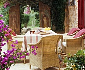 Frühstückstisch mit Rattansesseln auf mediterraner, sommerlicher Terrasse