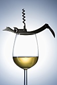 A glass of white wine with a corkscrew