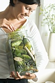 Young woman holding a large jar of pickled gherkins