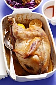 Whole roast chicken with honey and lemons in roasting dish