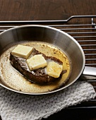 Steak with pieces of butter in a frying pan