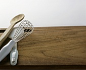 Whisk, salad server and wooden spoon on wooden board
