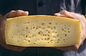 A pair of hands holding half a wheel of mountain cheese
