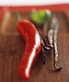 Vanilla pods and a red chilli pepper on a wooden board