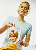 A young woman putting fruit in a blender
