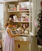 A girl standing in front of a crockery cupboard