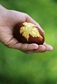 A decorated Easter egg with a leaf motif in someone's hand