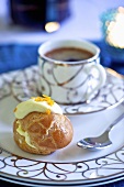 A profiterole with white chocolate and a cup of coffee