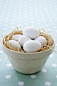 weiße Eier in einer Tonschale mit Stroh (Ostern)