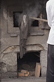 Baker taking bread out of old stone oven