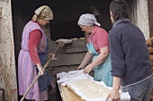 Countrywomen putting unbaked bread into old stone oven
