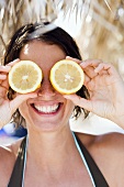 Young woman holding two lemon halves in front of her eyes