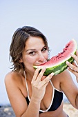 Junge Frau isst ein Stück Wassermelone am Strand