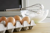 Stiffly beaten egg white in mixing bowl, egg tray