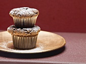 Two chocolate muffins dusted with icing sugar, stacked