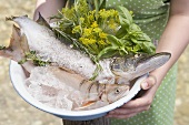 Woman holding bowl of freshly caught fish and herbs
