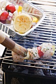 Brushing raw fish kebab on barbecue rack with oil