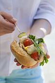 Woman putting grilled fish & vegetable kebab in baguette roll