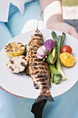 Woman holding plate of grilled fish and vegetables