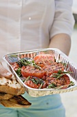 Woman holding an aluminium dish of grilled tomatoes