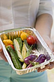 Woman holding barbecued vegetables in aluminium dish