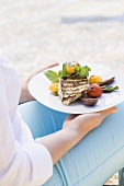 Woman holding plate of grilled fish & vegetables outdoors