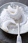 Vanilla crescents in dish of icing sugar with spoon