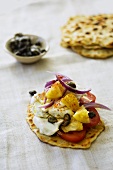 Naan bread topped with tomato, pineapple and capers