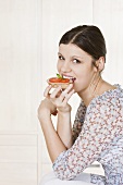 Young woman eating ham & tomato open sandwich (wholemeal)