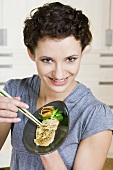 Young woman eating fried fish with chopsticks