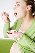 Schwangere Frau isst Joghurt mit Himbeeren