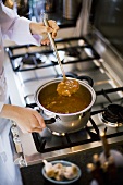 Female chef making vegetable soup on gas cooker