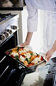 Köchin schiebt Backblech mit Gemüse in den Ofen