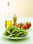 Fresh rocket on plate, olive oil, pepper mill, tomatoes