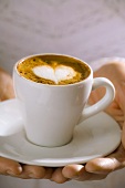 Frau hält Tasse Espresso Macchiato mit Herz im Milchschaum