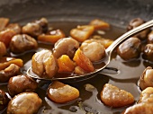 Glazed sweet chestnuts with dried fruit in frying pan