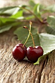 Two cherries with leaves on wooden background
