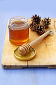 Pine honey in jar with honey dipper and pine cones