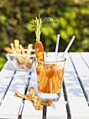 Carrot drink with grissini on summery garden table