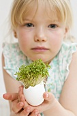 Little girl holding eggshell with cress growing in it