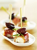 Bacon-wrapped soft cheese with olives on cocktail sticks