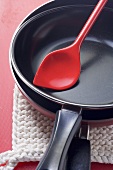 Two non-stick frying pans with red kitchen spoon