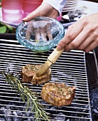 Brushing lamb chops on barbecue with oil