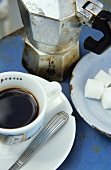 A cup of espresso, sugar cubes and espresso pot
