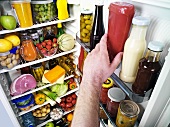 Hand greift zur Ketchupflasche in einem Kühlschrank
