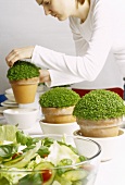 Junge Frau arrangiert Topfpflanzen auf einem Tisch mit Salat