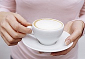 Frau hält eine Tasse Cappuccino (Bildausschnitt)